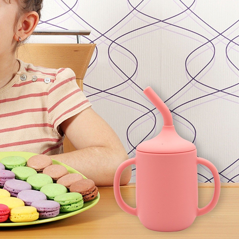 Pink silicone sippy cup placed on table with colorful macarons