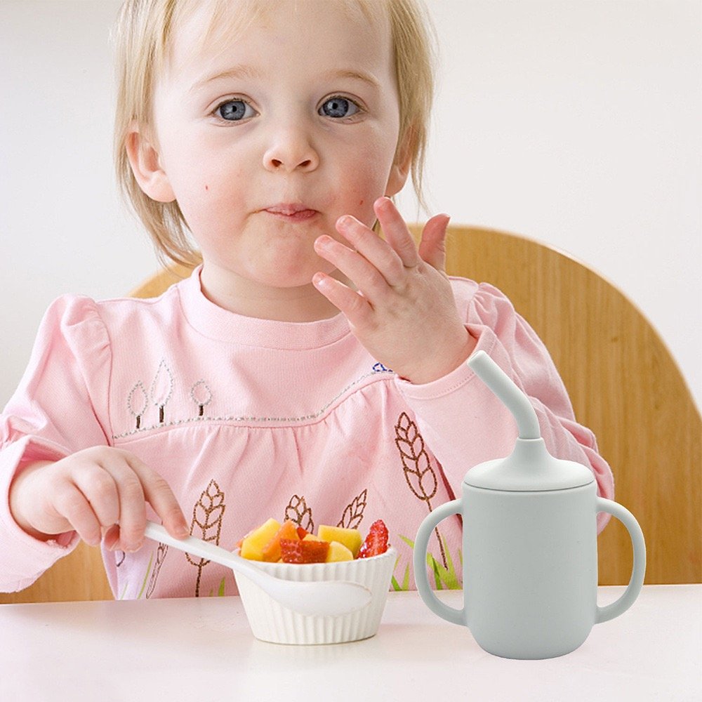 Silicone sippy cup beside child enjoying mealtime with fruits